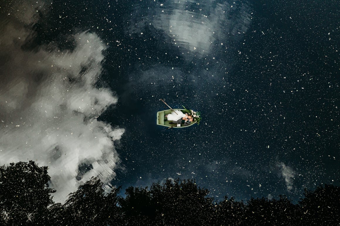 Couple de mariés sur une barque dans un lac qui reflète les étoiles de la nuit