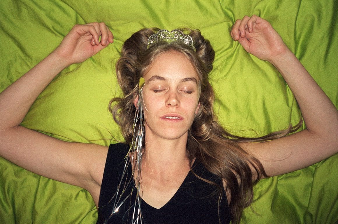 Jenny Rova allongée sur un lit vert avec une couronne 