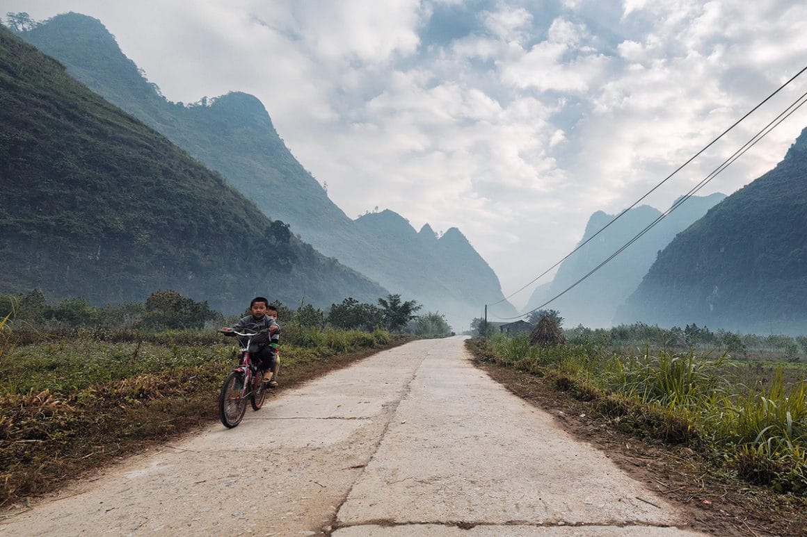 Voici une des impressionnantes photographies de Lukas Furlan :
Vue d'une route où l'on observe deux petits garçons faire du vélo de face. Ils sont encadrés par la montagne. on note la présente de câbles électrique à droite et des nuages dans le ciel bleu.