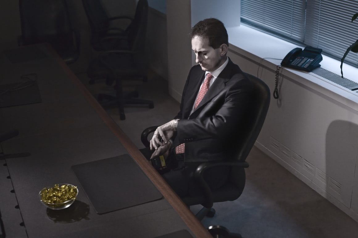 Kristoffer Axén, un personnage qui regarde sa montre, installé à son bureau. 
