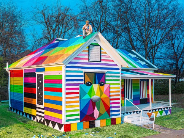 Okuda sur le toit de la maison qu'il a peinte dans le cadre du projet " The Rainbow Embassy " 