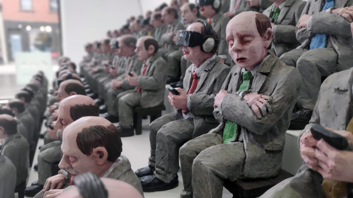 Isaac Cordal, détail de l'assemblée assises de petits personnages. Un des personnages a un casque de réalité virtuelle. 