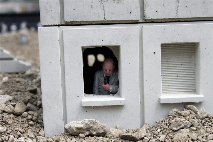street art, un homme miniature à une fenêtre devant des gravas. 
