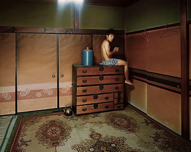 Yoshiki Hase, un homme sur une commode dans un intérieur japonais. 