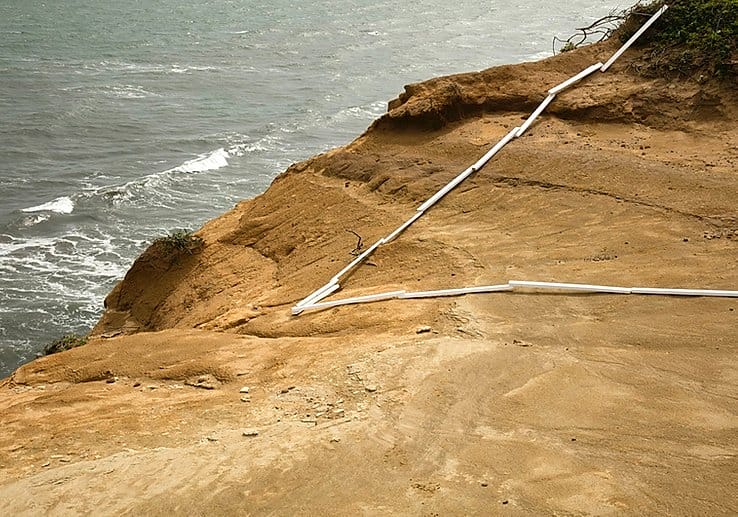 Une installation avec des planches blanches sur un paysage de falaise en terre devant la mer. 