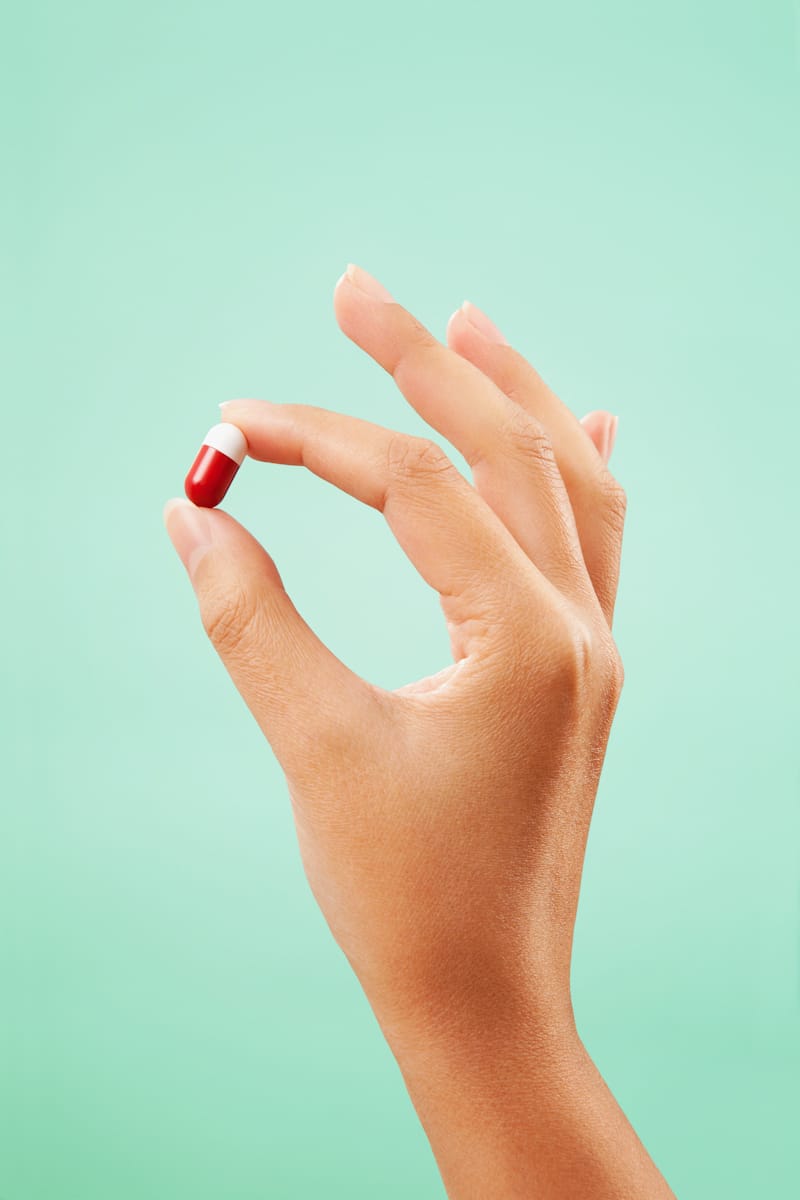 Une main sur fond bleu tenant une pilule rouge et blanche. 