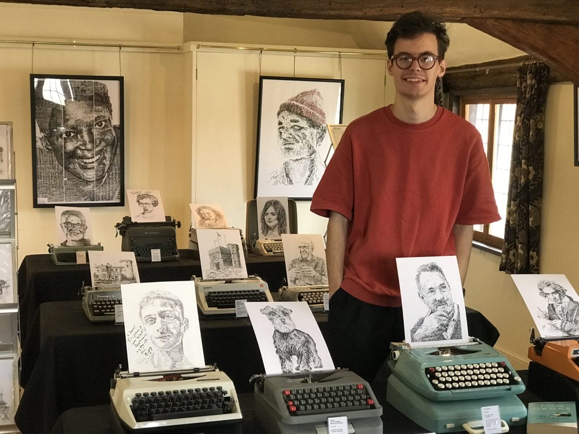 L'artiste James Cook au milieu de certaines de ses œuvres, réalisées à la machine à écrire, lors d'une exposition