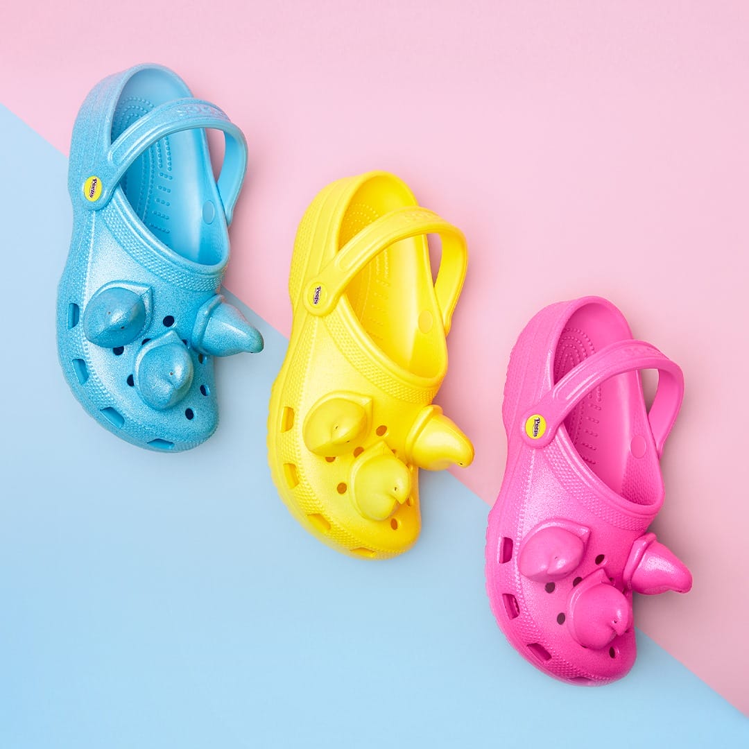Photographie de trois crocs, jaune, rose et bleu sur fond rose et bleu pastel