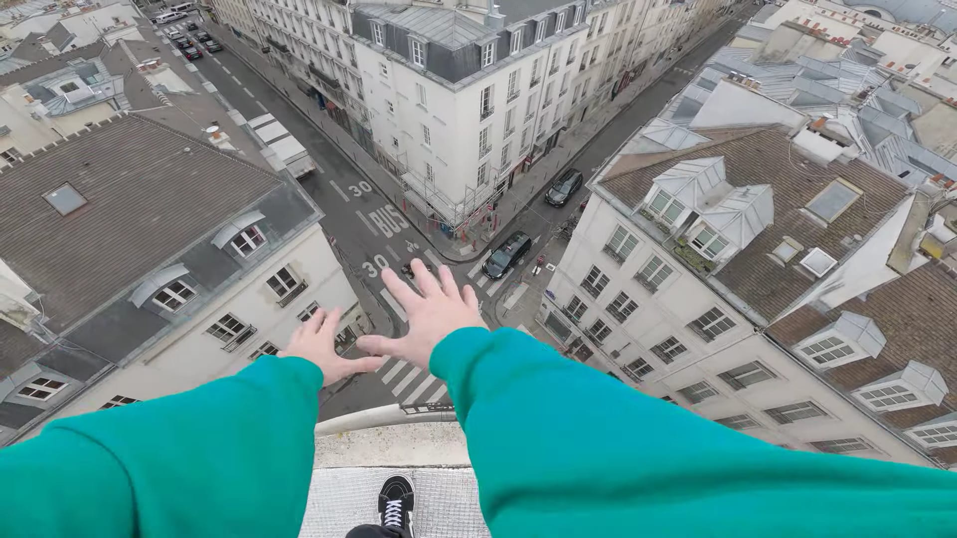 Vue sur les rues de Paris depuis les toits, o voit les bras d'un homme et son pied, au bord du toit