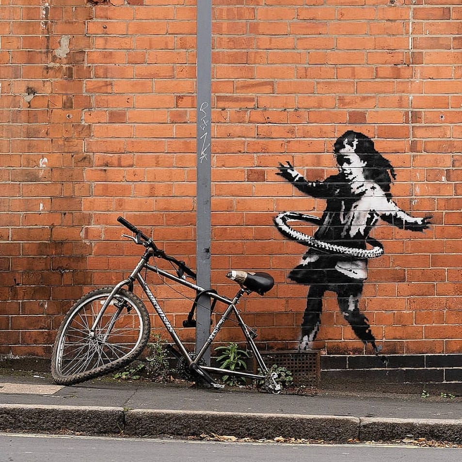 Mur en brique rouge, pochoir de Banksy d'une petite fille qui joue avec un pneu comme cerceau Fille au hula-hoop