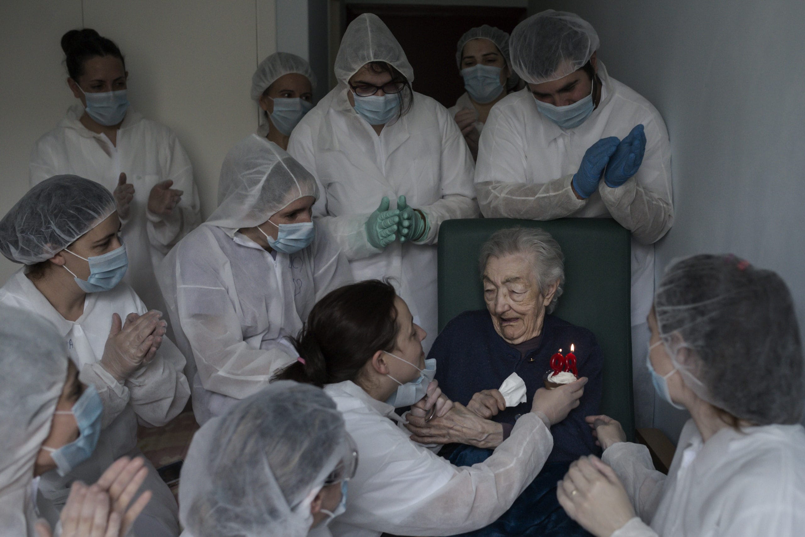 Une personne âgée qui fête son 98e anniversaire est entouré de soignants masqués