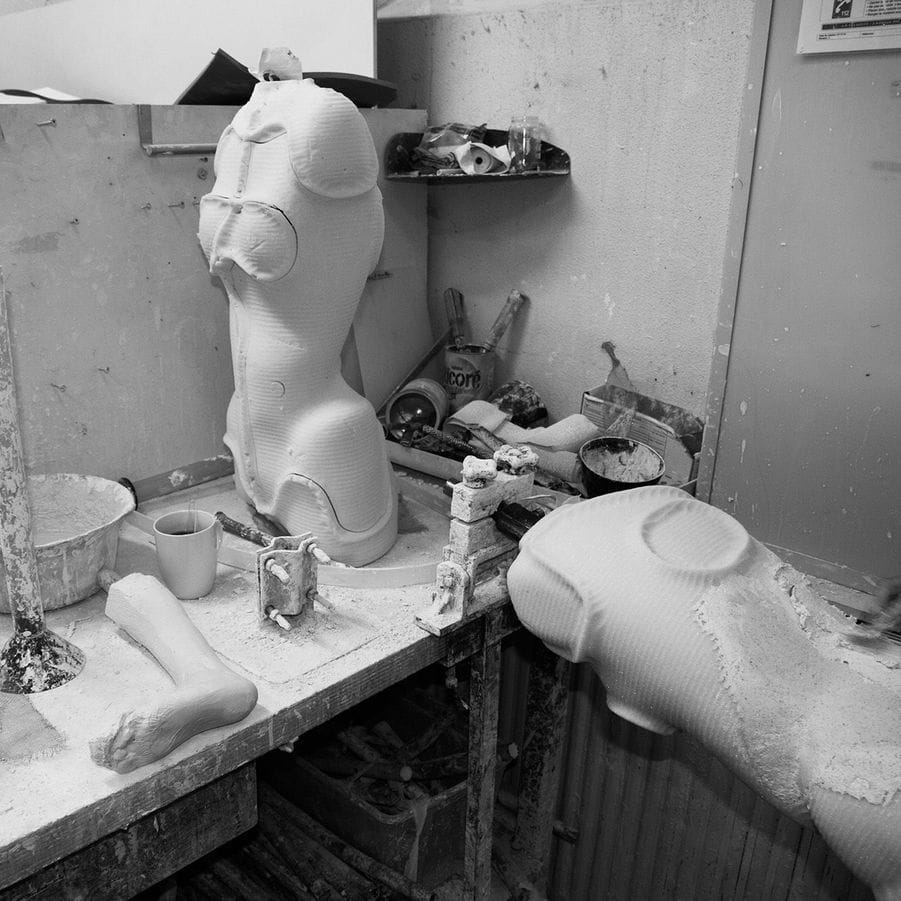 Photographie en noir et blanc de l'atelier où sont fabriqués les corsets médicaux, bustes de mannequins posés sur l'établi
