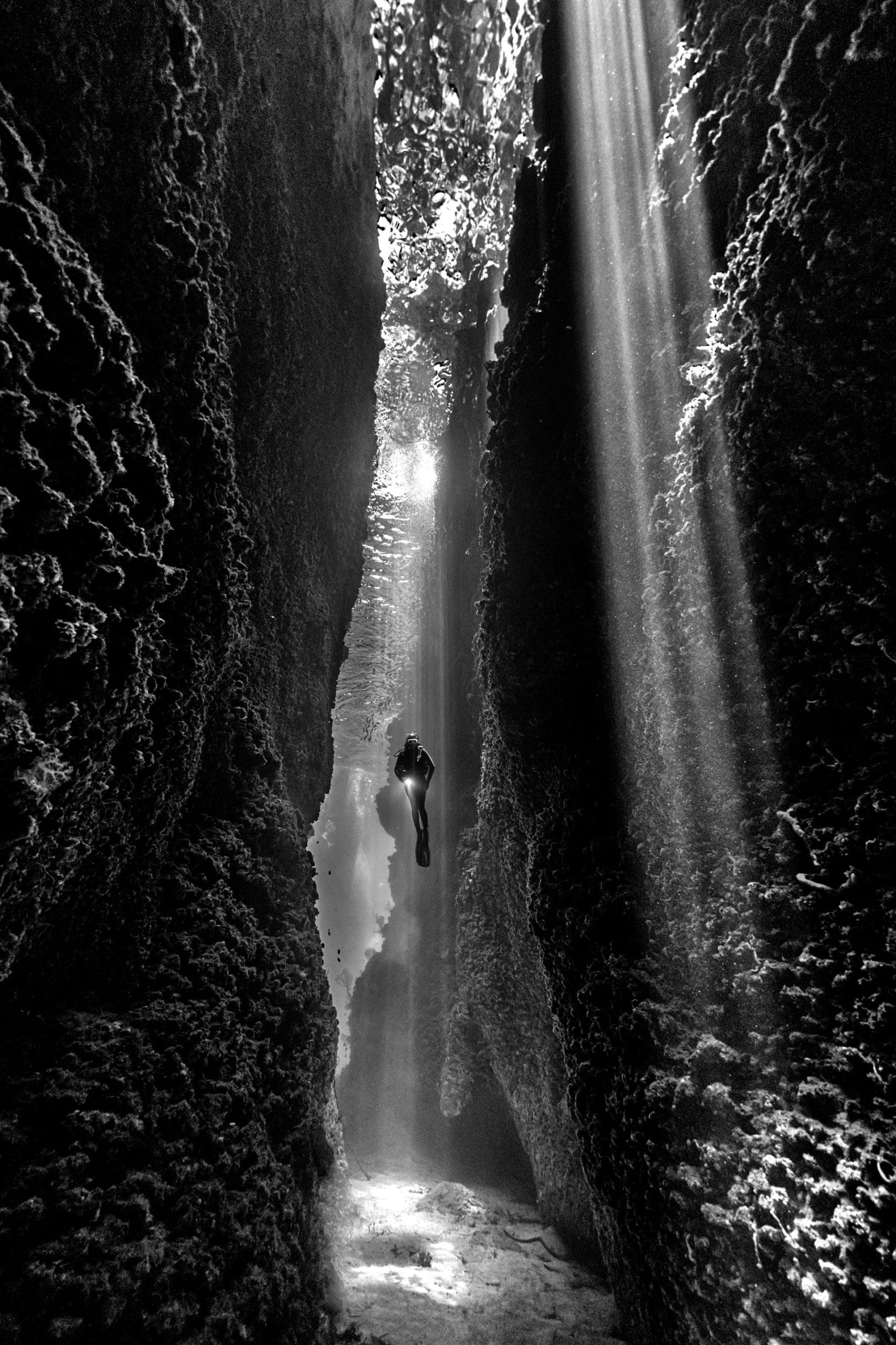Photographie en noir et blanc, un plongeur et au milieu de deux énormes rochers