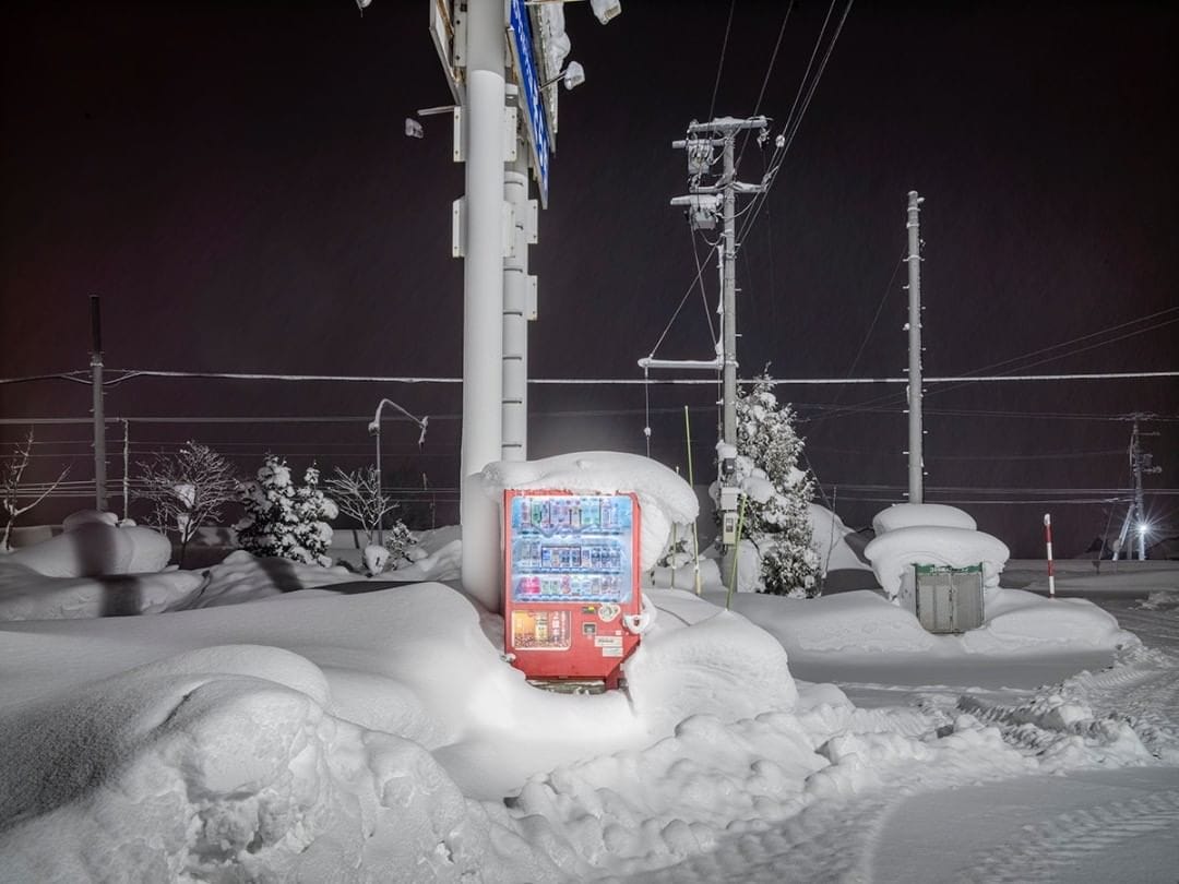Un distributeur est au pied d'un poteau électrique, la neige l'envahit