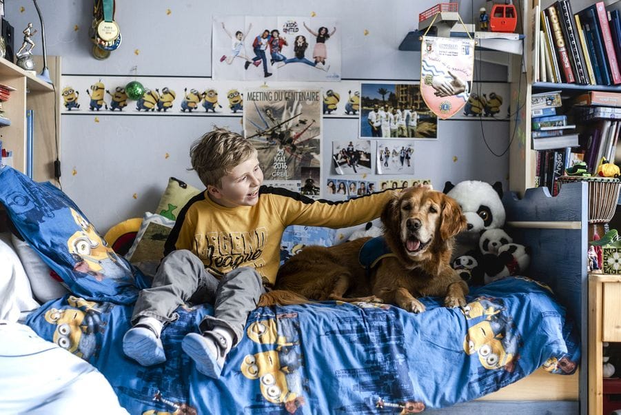 Jeune garçon qui caresse son chien, assis tous les deux sur son lit.