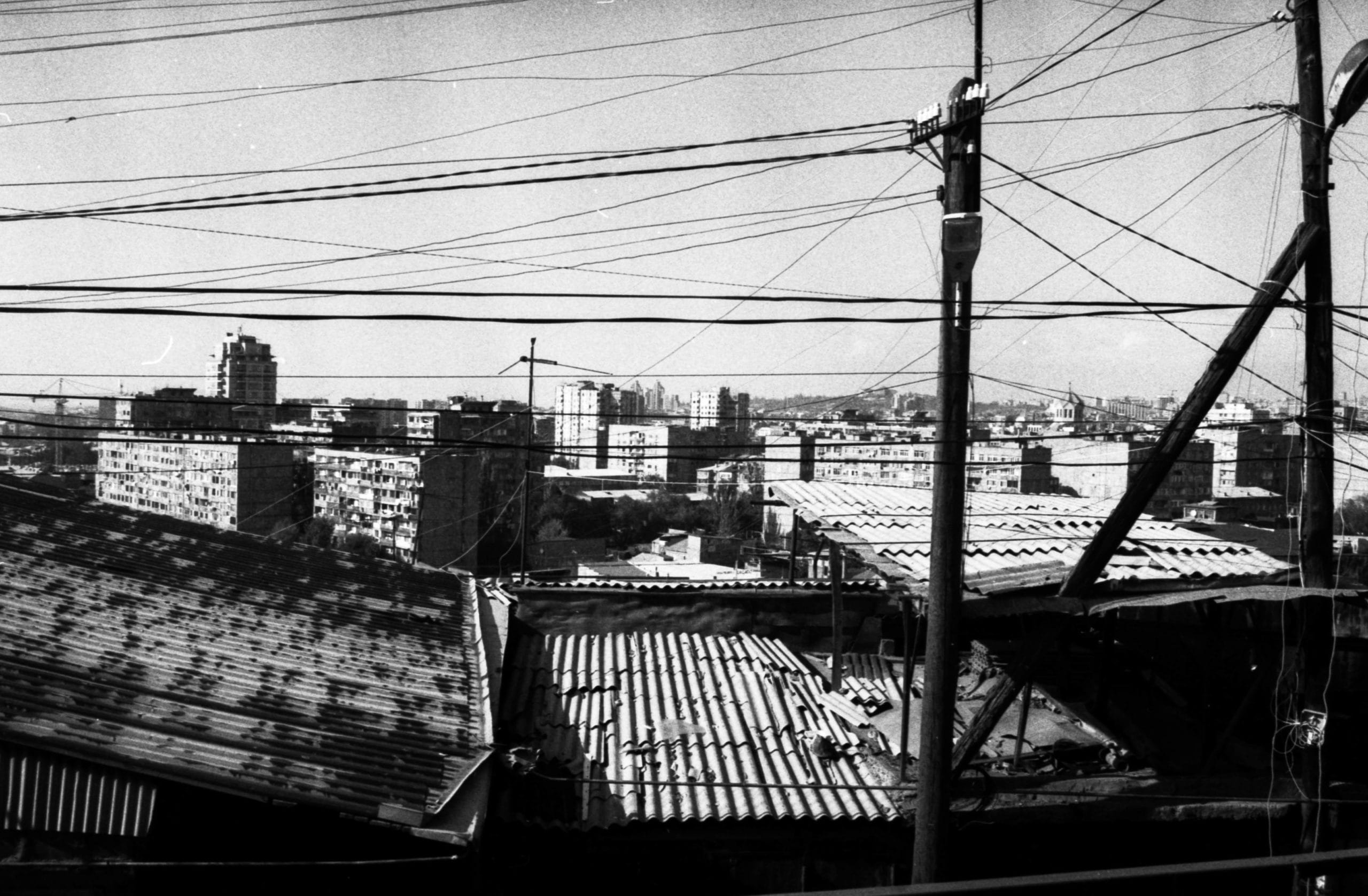 Photographie en noir et blanc, vue sur des toits en tôle et de multiples câbles électriques