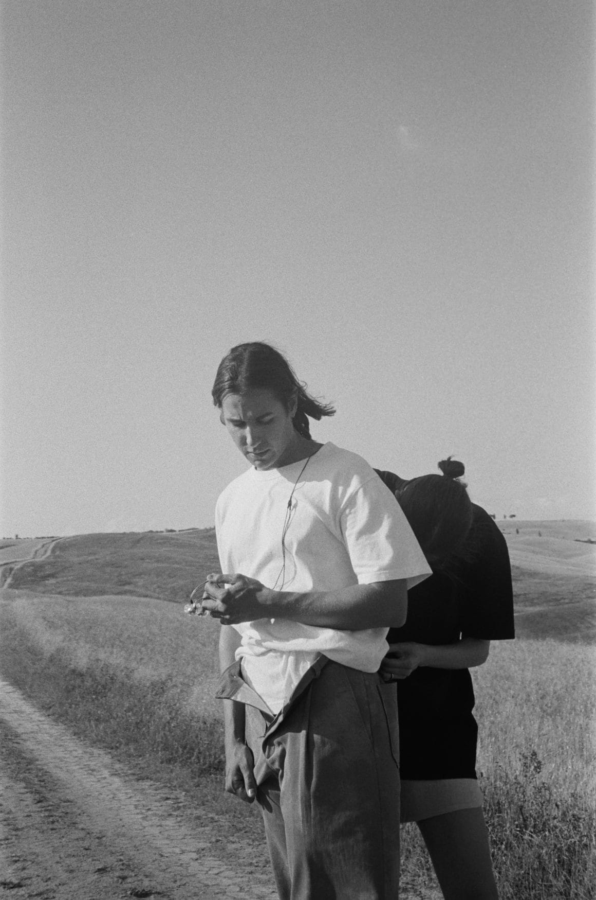 Photo en noir et blanc, un homme se tient debout et une personne derrière ajuste son micro