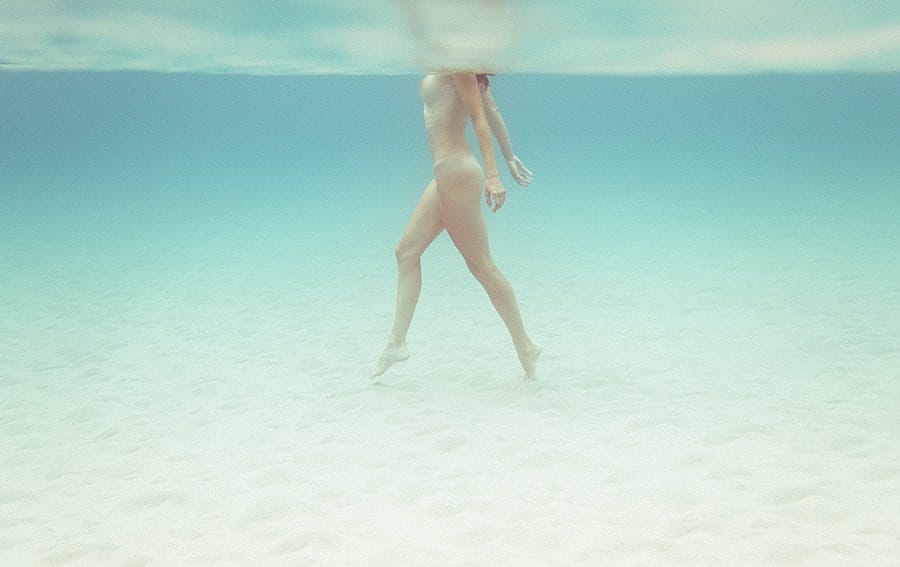 Photographie prise sous l'eau, on voit une femme nue marcher sur le sable