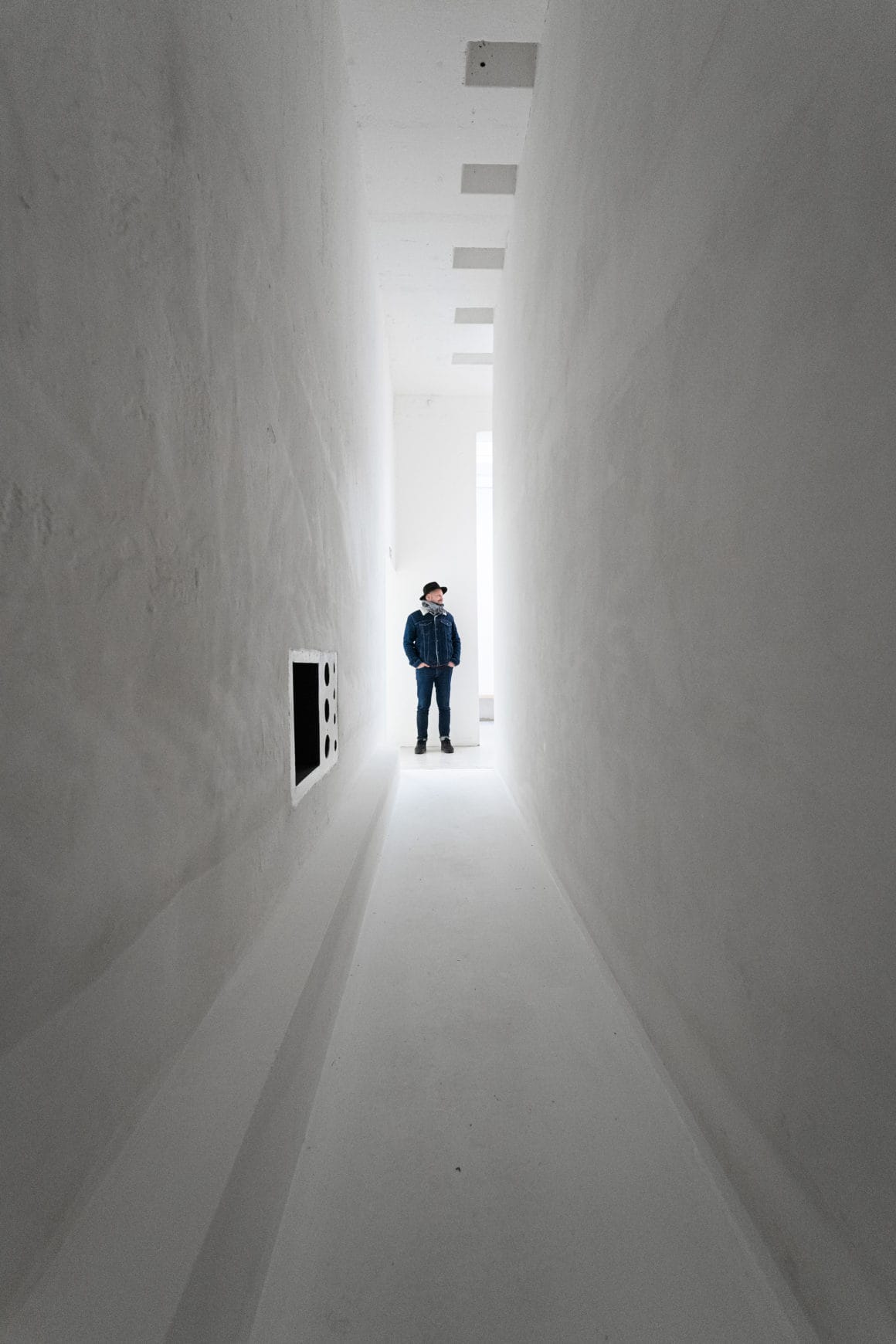 Photo d'un long couloir aux murs blancs au bout duquel il y a un homme