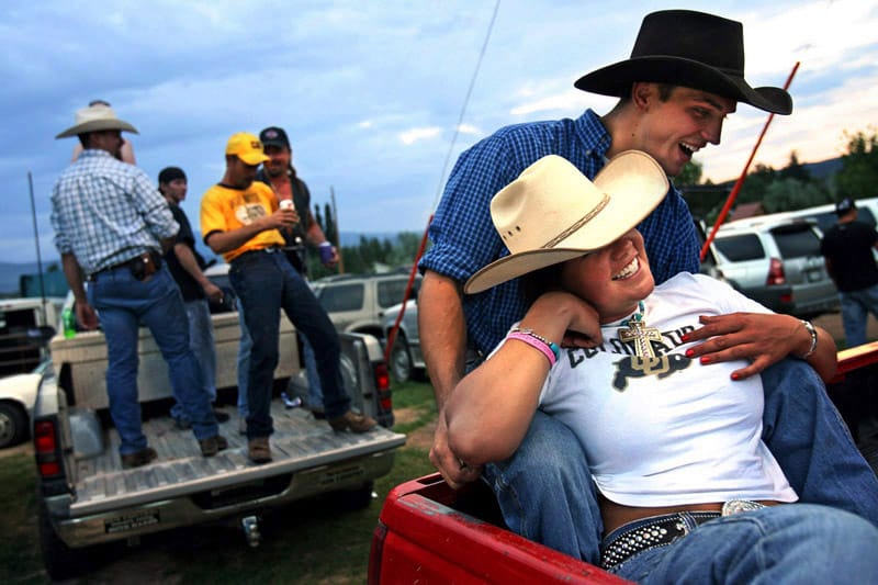 Deux jeunes s'enlacent, pendant que d'autres enchaînent les canettes sur le dos de leur pick-up. Tous rient, et sont vêtus de t-shirt ou de chemises à carreaux, avec des jeans et des chapeaux de cow-boys.