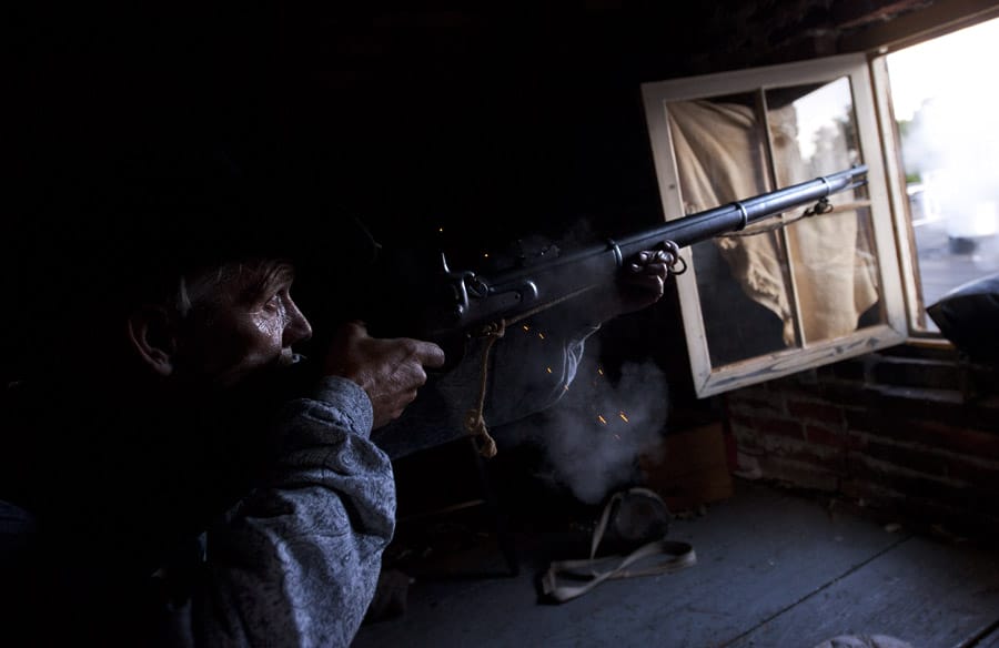 Un homme tire avec un fusil ancien depuis un baraquement. Clair-obscur.