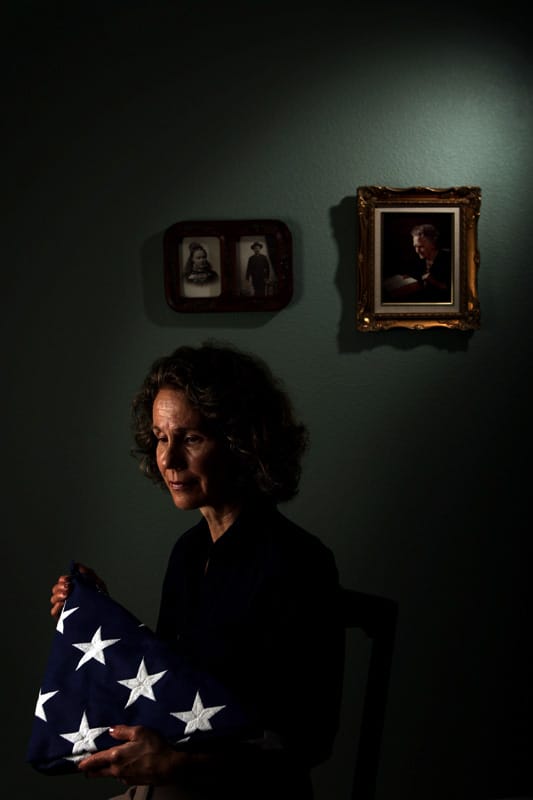 Une veuve tient dans ses bras le drapeau américain remis lors des obsèques publiques de combattants. Derrière elle, des portraits anciens.