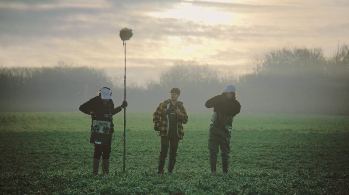Les trois personnages se préparent à enregistrer les sons de la nature, dans un champs au petit matin.