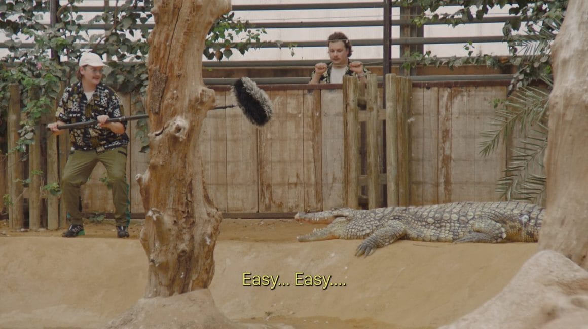 Myd enregistre un crocodile dans une cage spéciale. Un autre personnage le regarde avec inquiétude.