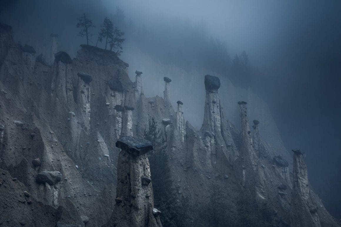 Bord de montagne, brouillard noir. Le sol a été comme mangé, laissant des pics abrupts se distinguer, avec des pierres noires à leur sommet.