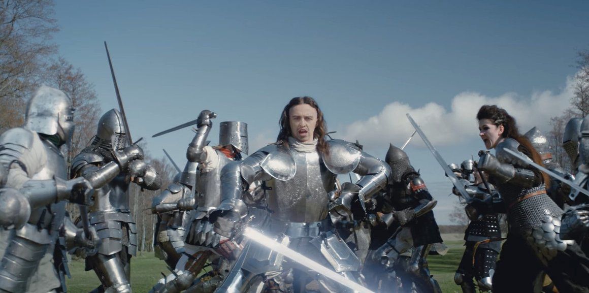 Le rappeur, en armure, se tient au centre d'une bataille, avec les armées se lançant au combat de part et d'autres de l'écran.