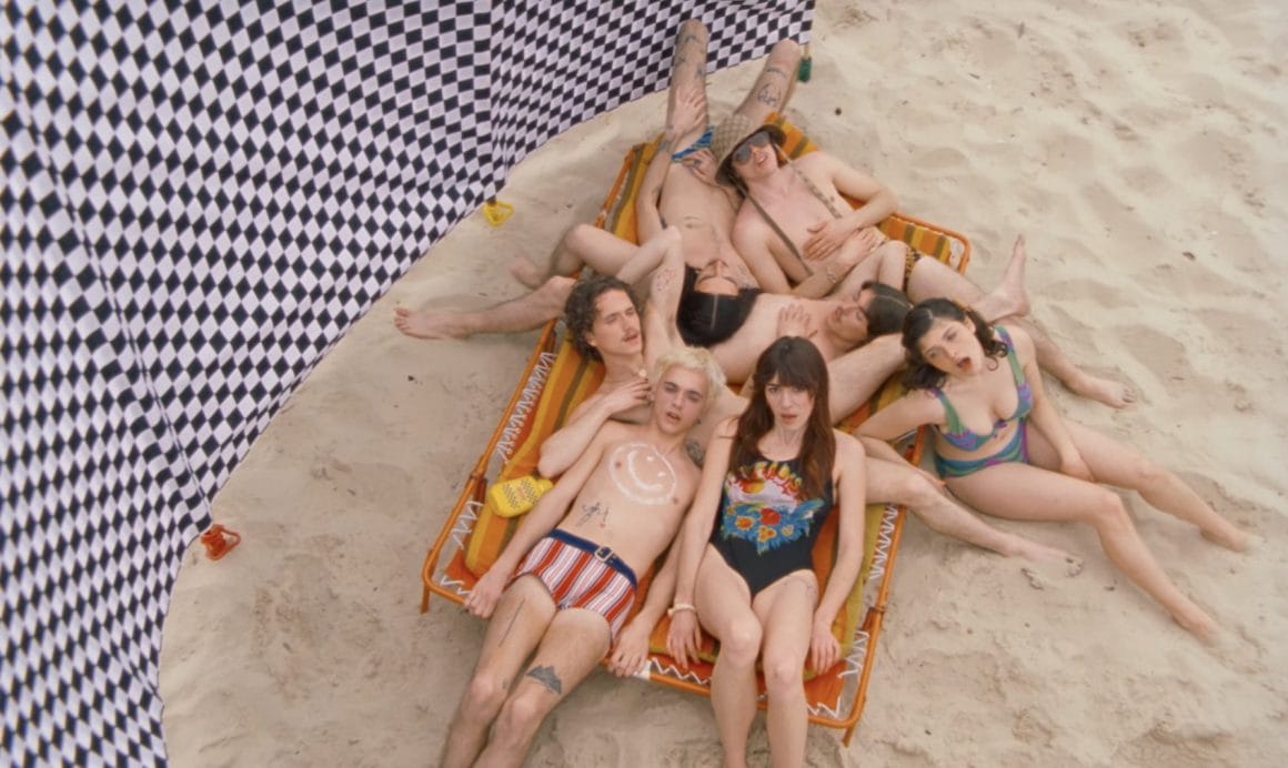 Les sept membres sont allongés sur un lit de plage, les corps entremêlés.
