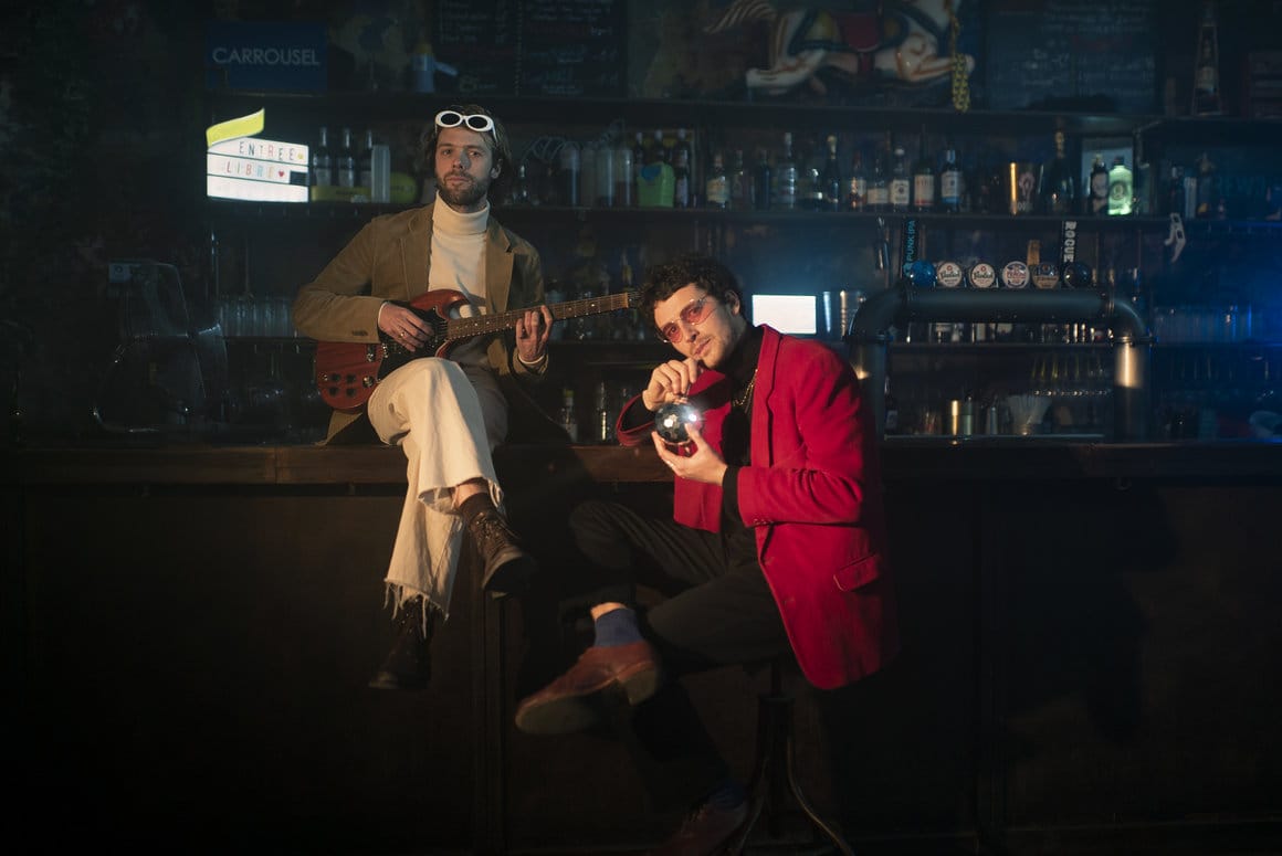 Dans un bar sombre tiré du clip "Dehors", Ludovic Bailly à droite est assis sur le comptoir, sa guitare sur les genoux. A gauche, Emmanuel Jarrige sirote un cocktail dans une mini boule à facette, accoudé au comptoir.