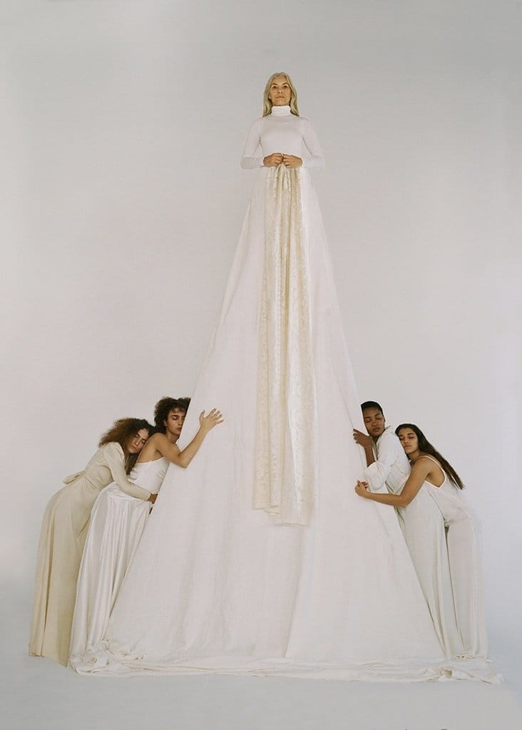 femme âgée avec une très longue robe blanche entourée de 4 femmes qui l'enlacent