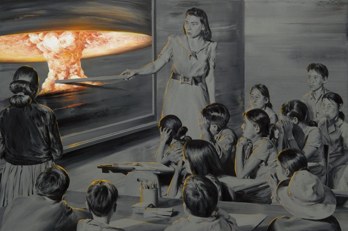 Une salle de classe bondée est orientée vers un tableau, où la maîtresse pointe de sa règle une explosion nucléaire.
