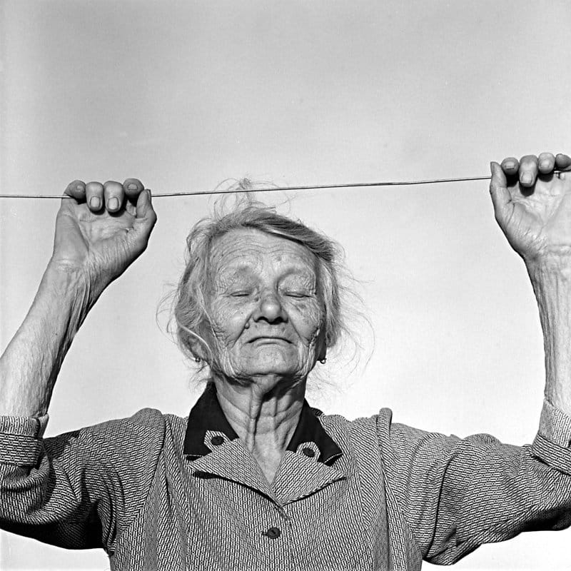 Photographie d'une vieille femme qui se tend à une corde à linge.