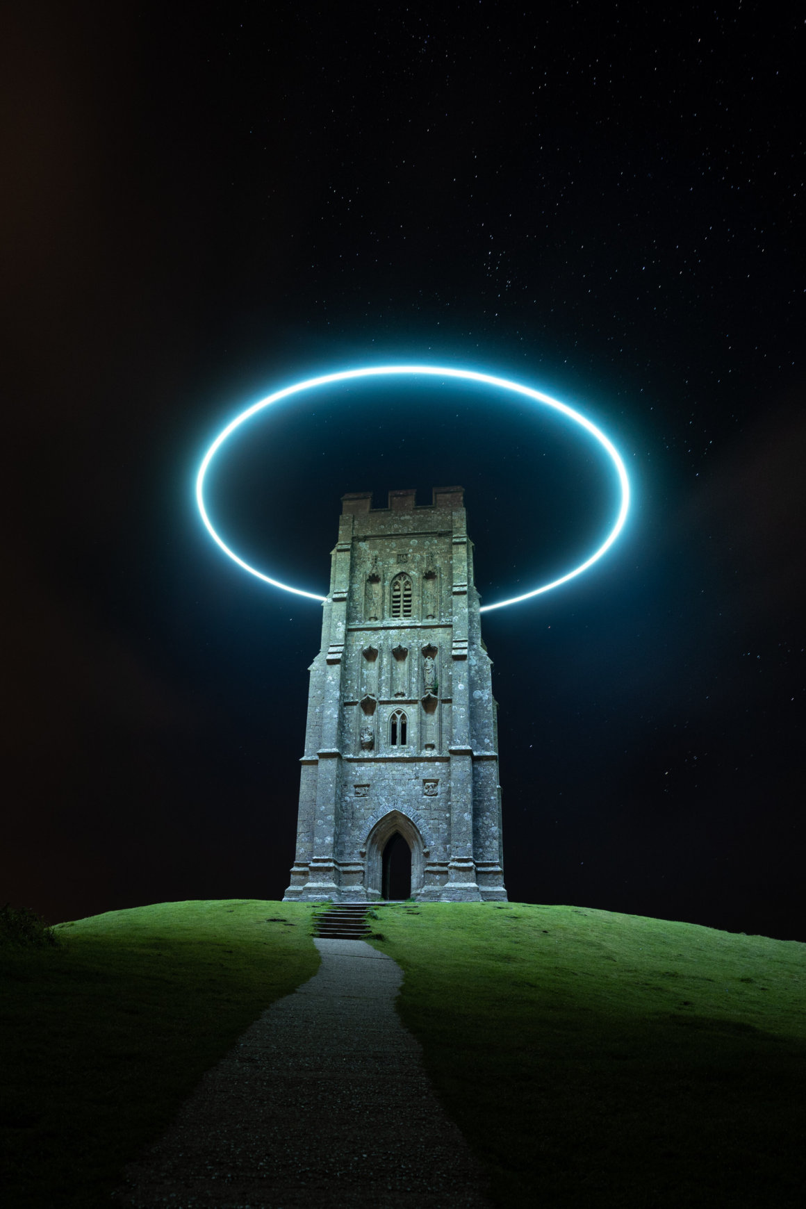 la tour de glastonbury photographié de nuit, entourée d'un halo lumineux qui l'éclaire