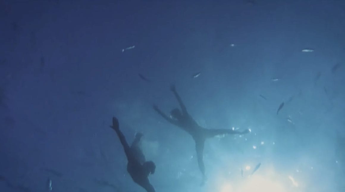 Extrait du clip "Aller Simple". Cadre en contre plongée, depuis les fonds marins. On distingue les silhouettes des nageurs.