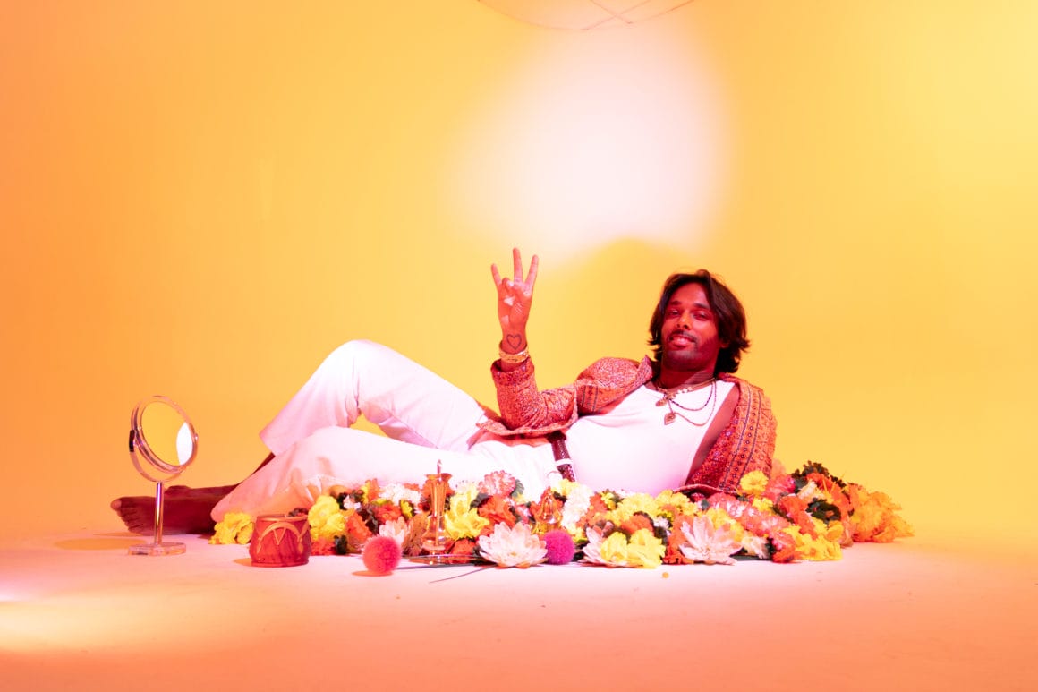 un deux le dj qui réinvente un mantra avec son nouveau titre Ganapataye
ici l'artiste est allongé sur un lit de fleurs en faisant un signe de paix de ses mains. 