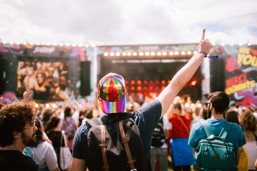 Un homme de dos avec une casquette chromée multicolore pointe un doit en l'air. Autour, des festivaliers face à la scène des Solidays, l'un des festivals incontournables de 2022.