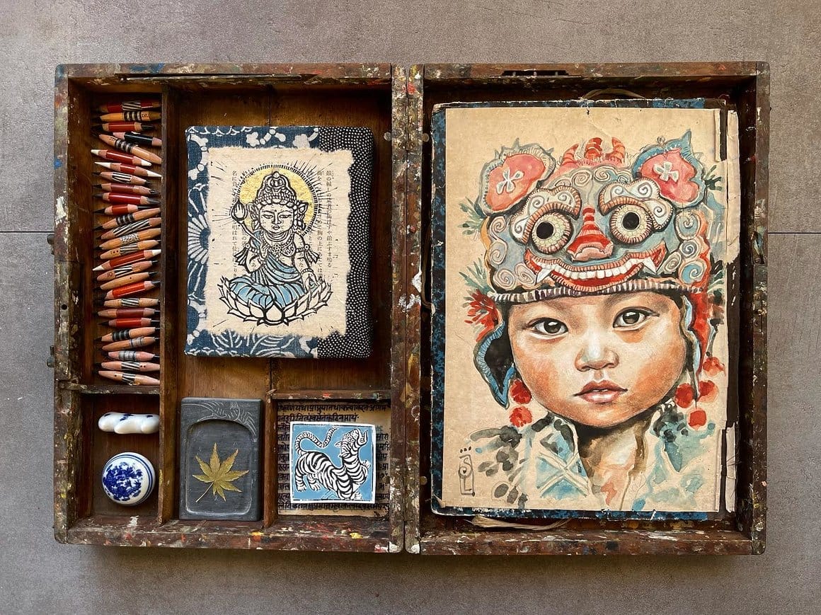 Boite à trésor avec le dessin d'un bébé chinois du Yunnan avec un bonnet traditionnel, brodé tigre pour faire fuir les mauvais esprits, des bouts de crayons, le dessin d'une divinité, des outils, etc.