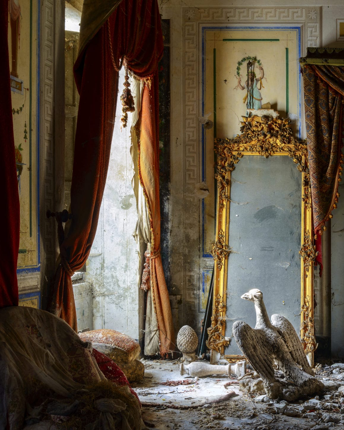 Partie d'une pièce abandonnée avec de longs rideaux rouges, un miroir et d'autres objets à terre