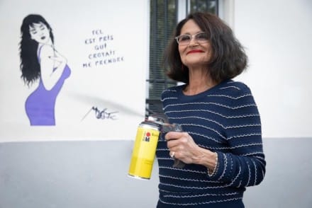 Photo de Miss.Tic - street artist avec une bombe à la main et un graffiti derrière elle