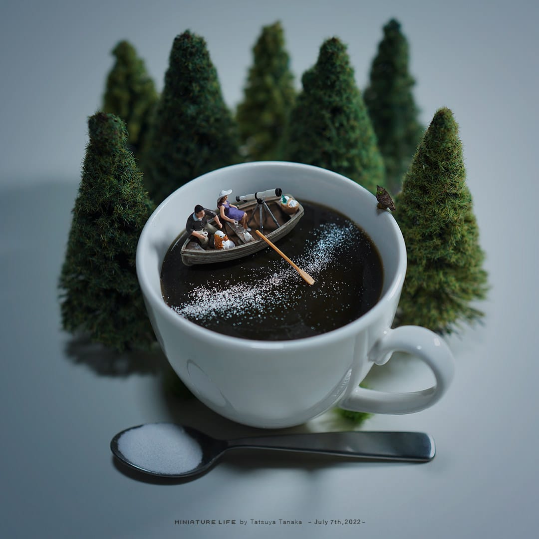Ce diorama représente des personnages dans une barque placée dans une tasse de café avec des sapins autour de la tasse.