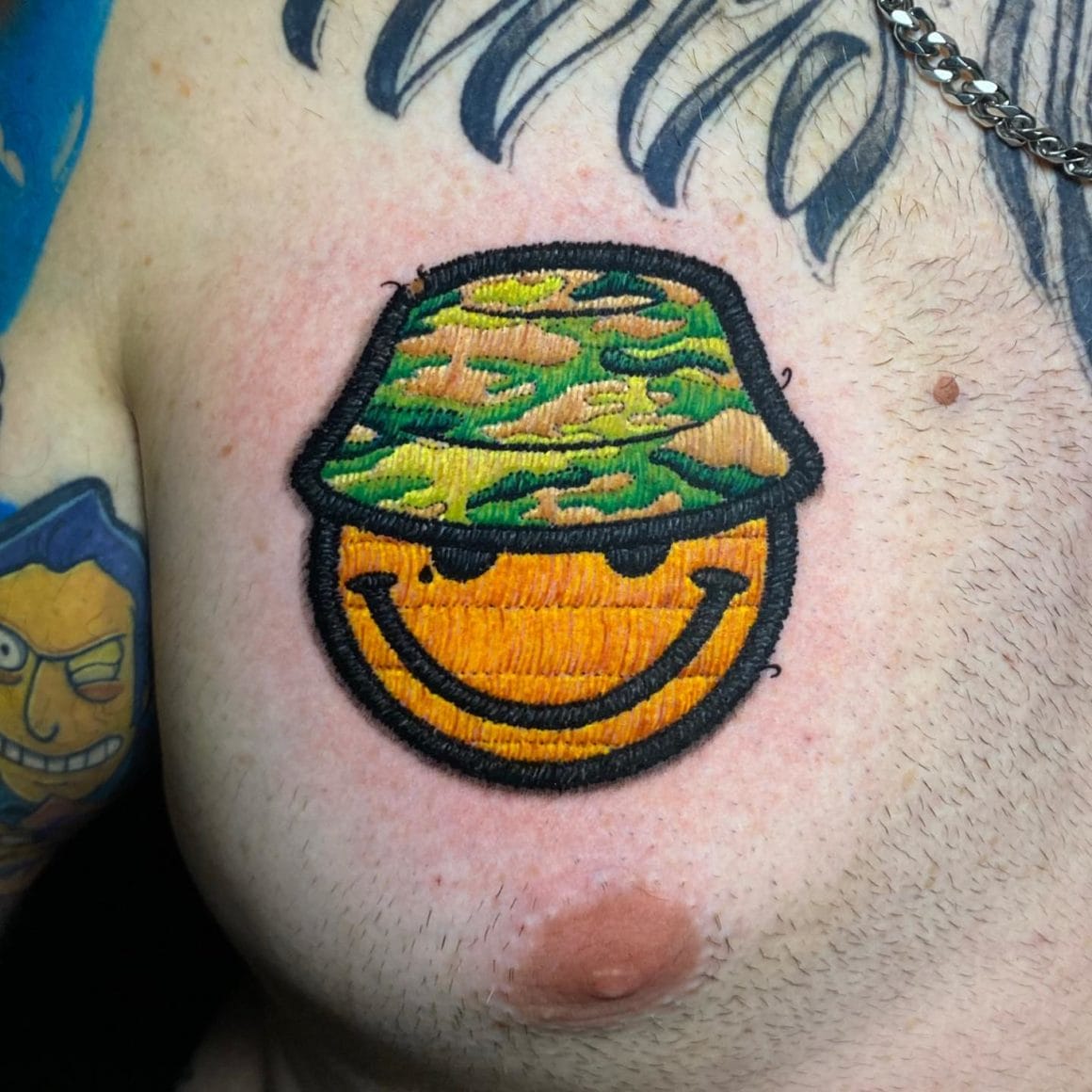 Ce tatouage représente un smiley avec un bob à motif militaire.