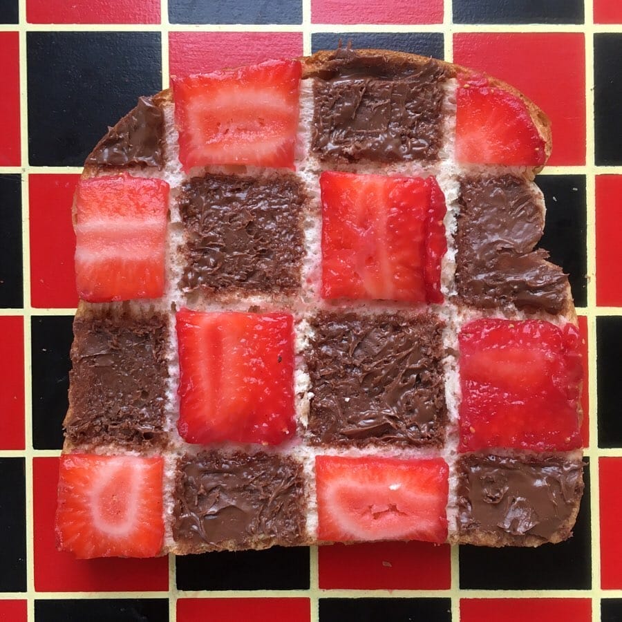 Oeuvre illusionniste représentant une tartine de chocolat et de fraise assorti à la table à carreaux rouge et noir juste en dessous.