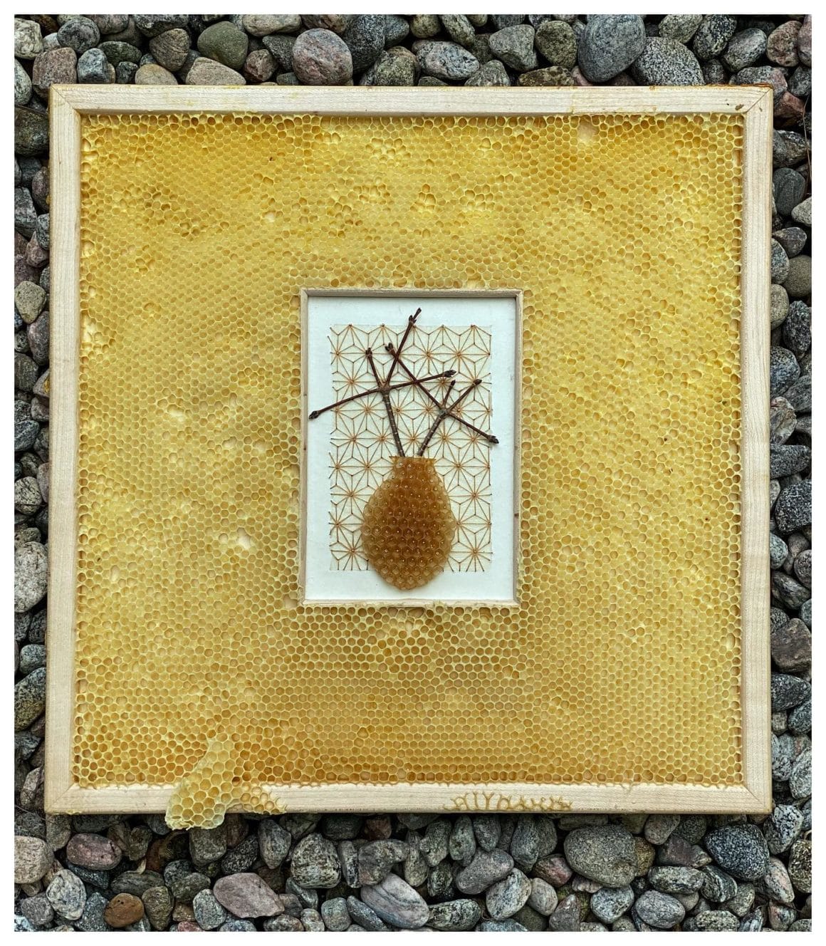 Cadre en bois avec des formes géométriques, des branches et un bout de ruche cousu sur du papier japonais. L'oeuvre est disposé dans une véritable ruche vide d'abeilles.