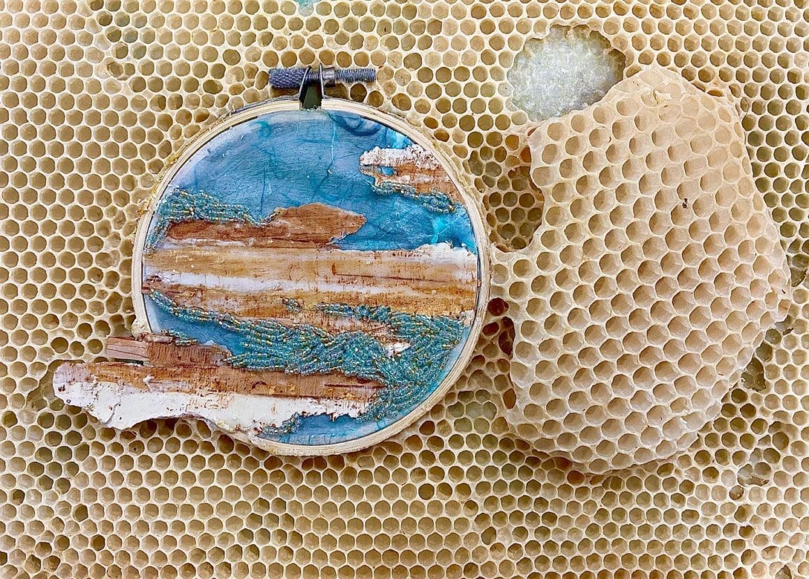 Cercle brodé avec des perles et un motif bleu ainsi que des écorces d'arbre. Le tout est intégré dans une ruche