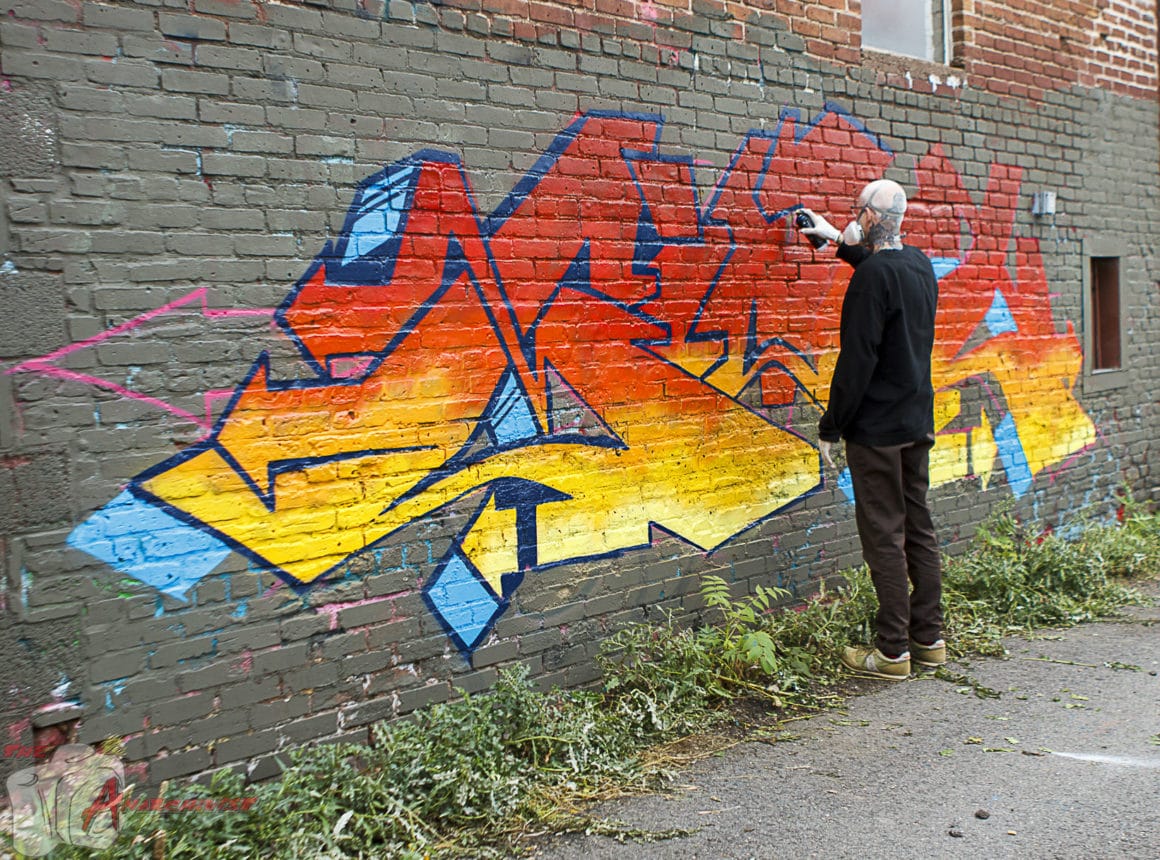 Mike Giant, une bombe aérosol à la main, en train de faire un graffiti sur un mur.