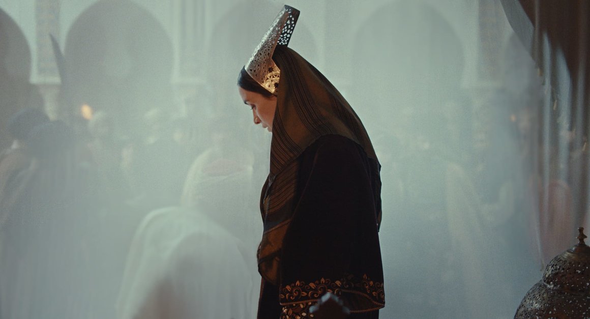 Photographie qui sert d'affiche du film La Dernière Reine. Adila Bendimerad, au centre du  cadre, se tient seule, debout face à un voile qui la sépare de la foule. 