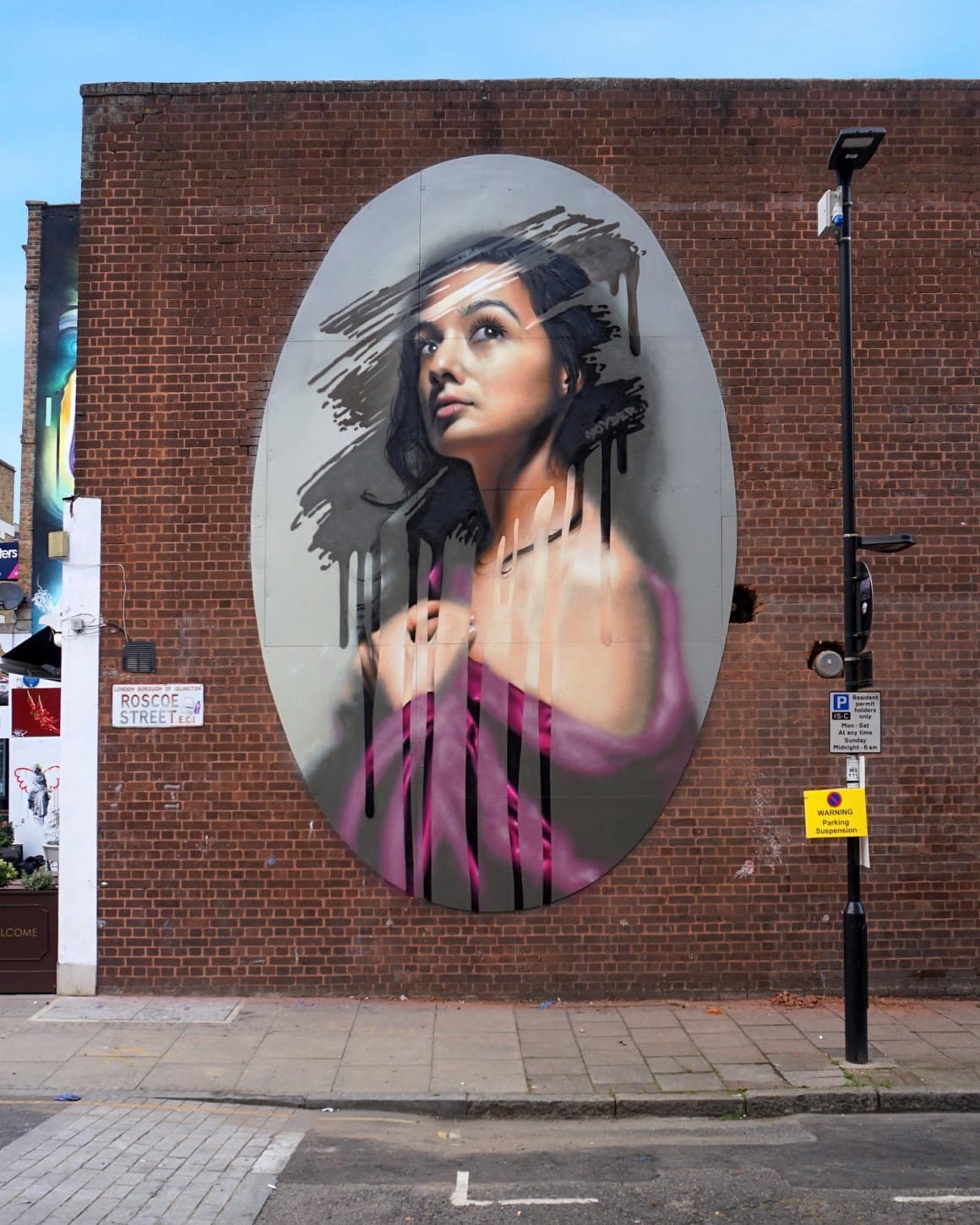 grande peinture murale de forme ovale rappelant un cadre, sur un mur dans la ville, avec une femme et une impression de traces faites sur une fenêtre couverte de buée